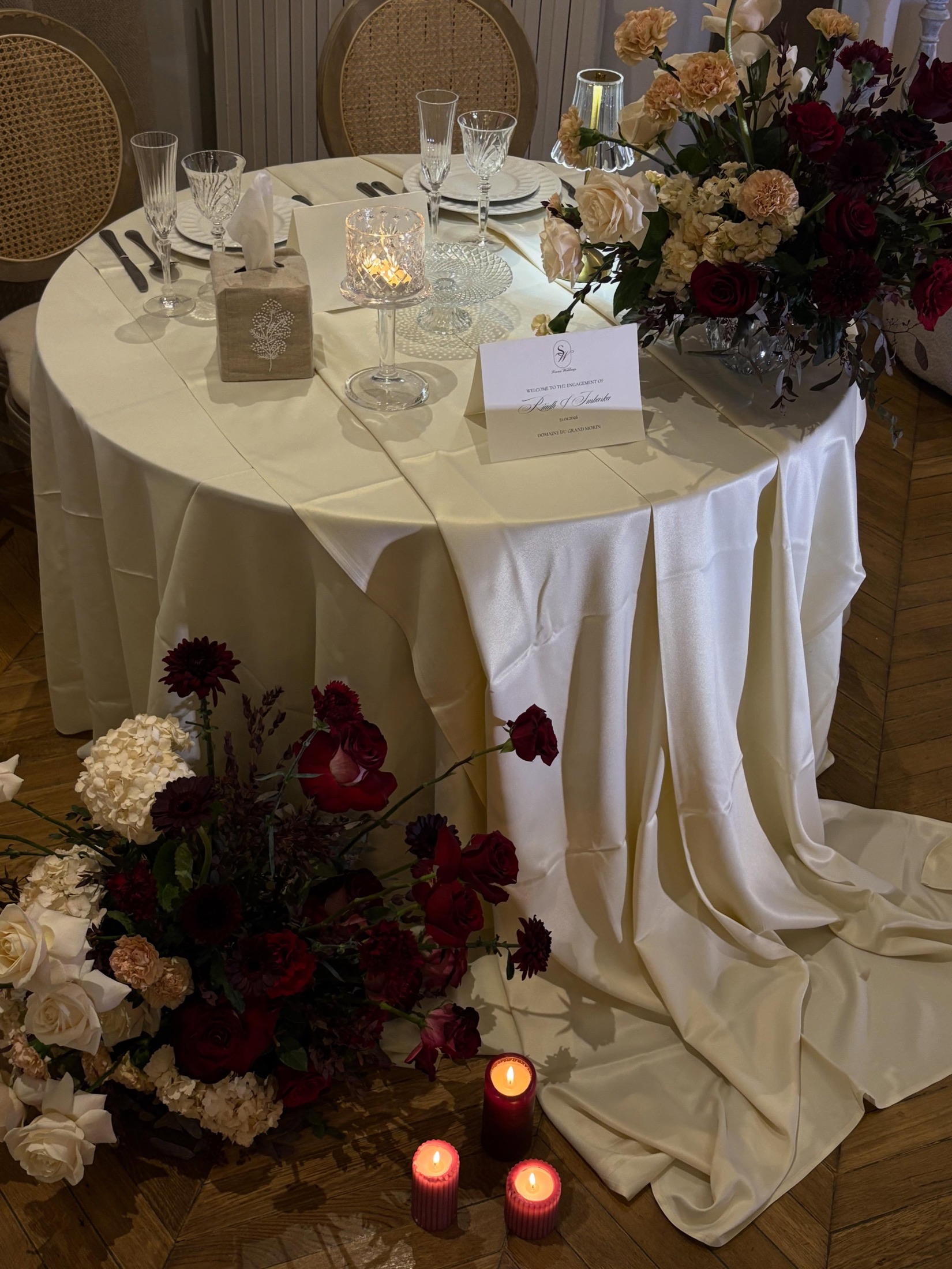 Table ronde nappée d'ivoire, composition de fleurs bordeaux au sol et bougies allumées