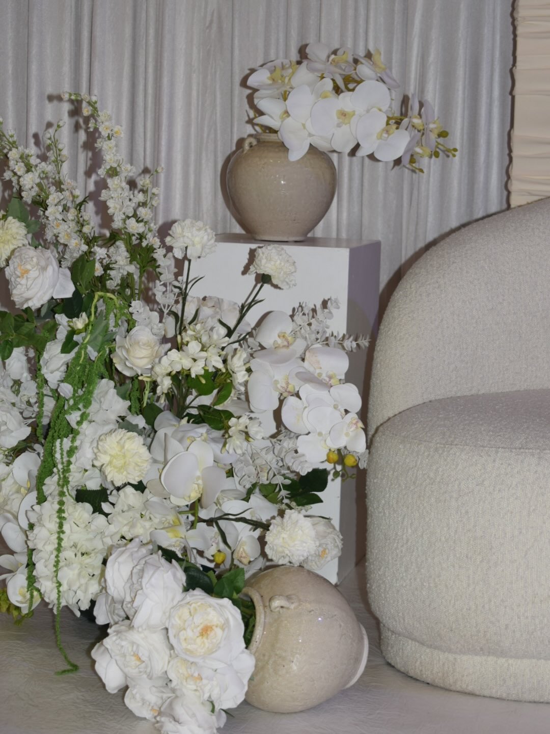 Salon blanc : fauteuil en bouclette, vase en céramique et cascade d'orchidées et de roses blanches